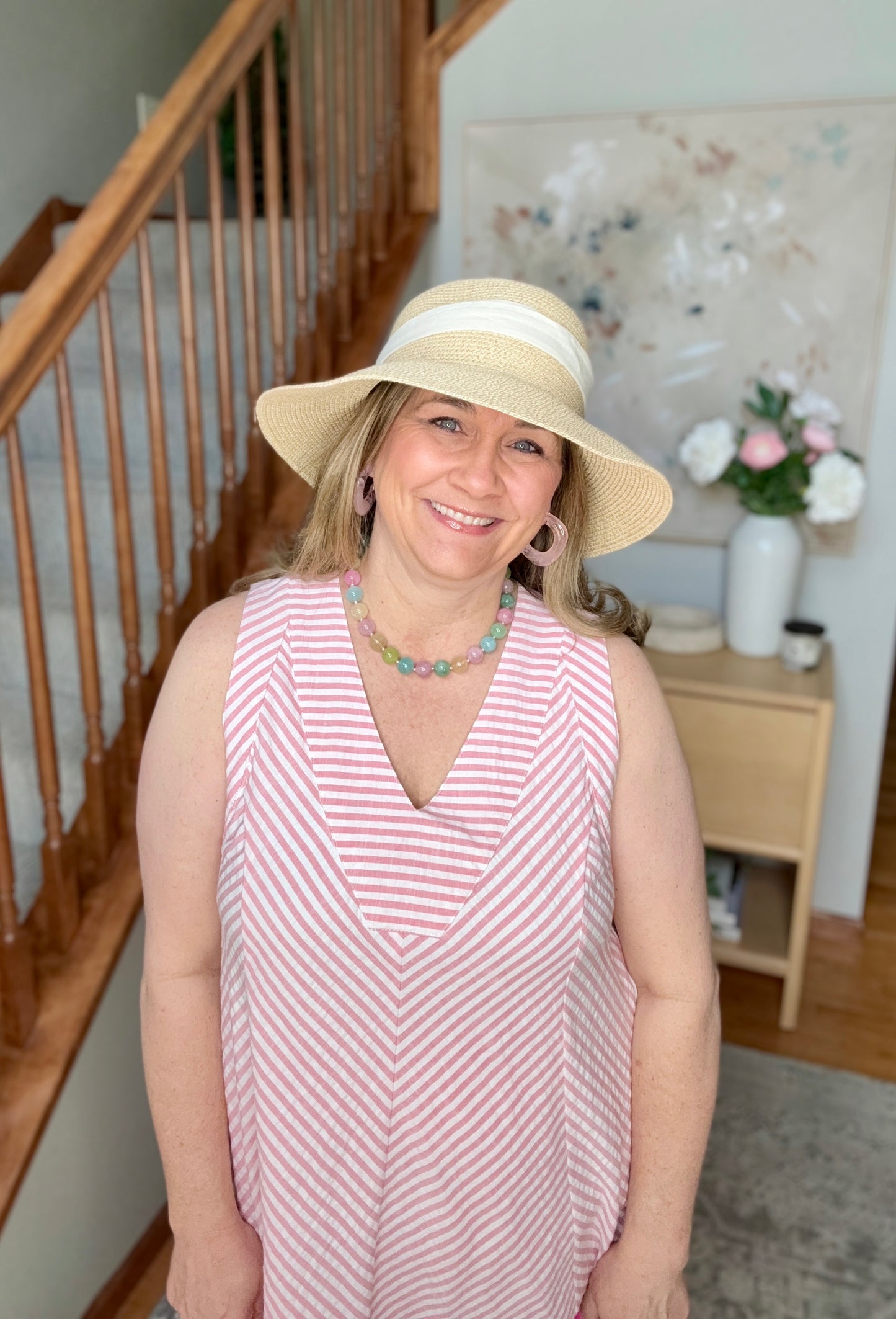 Woman wearing a pink and white striped dress and a beige hat indoors.