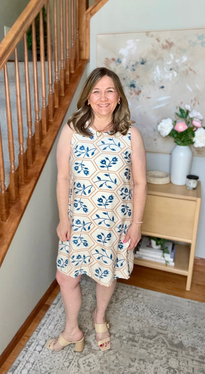 Woman in a floral dress standing in a home interior with a staircase and decorative items.