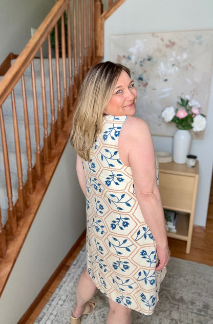 Woman in a floral dress standing in a home setting with a staircase and decorative items.