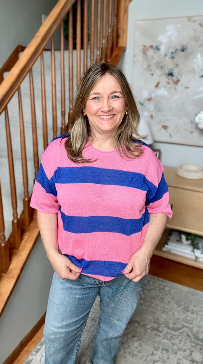 Woman wearing a pink and blue striped sweater standing in a home setting.