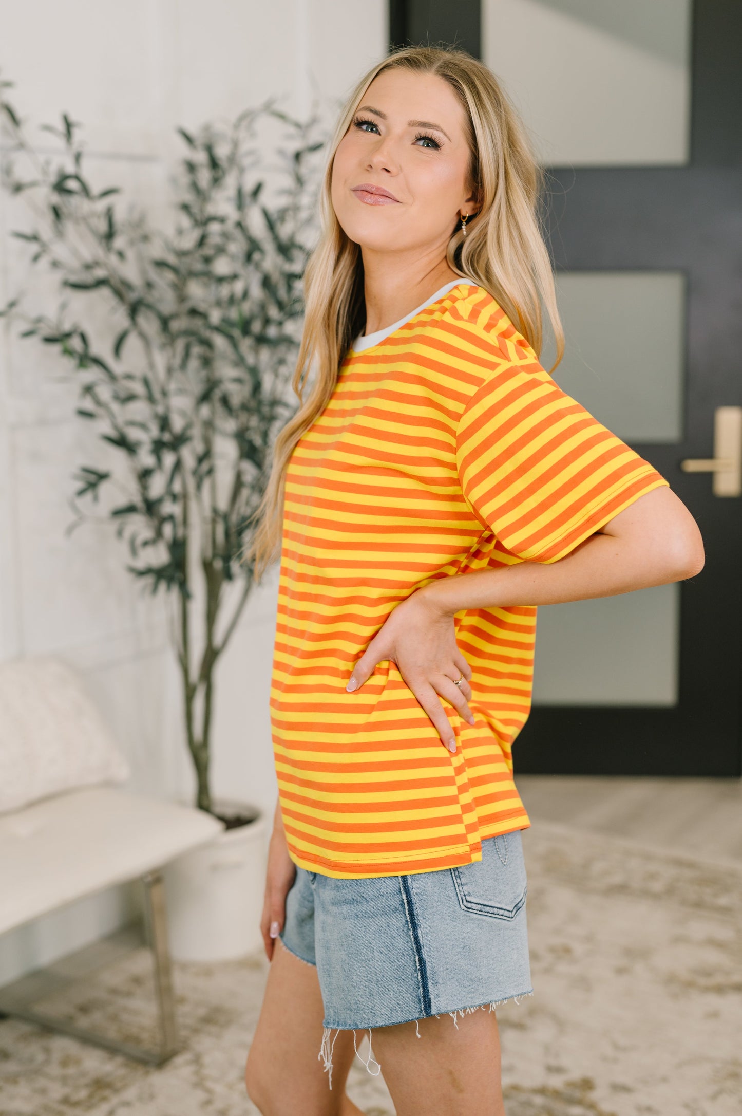 Woman wearing a yellow striped shirt and denim shorts indoors.