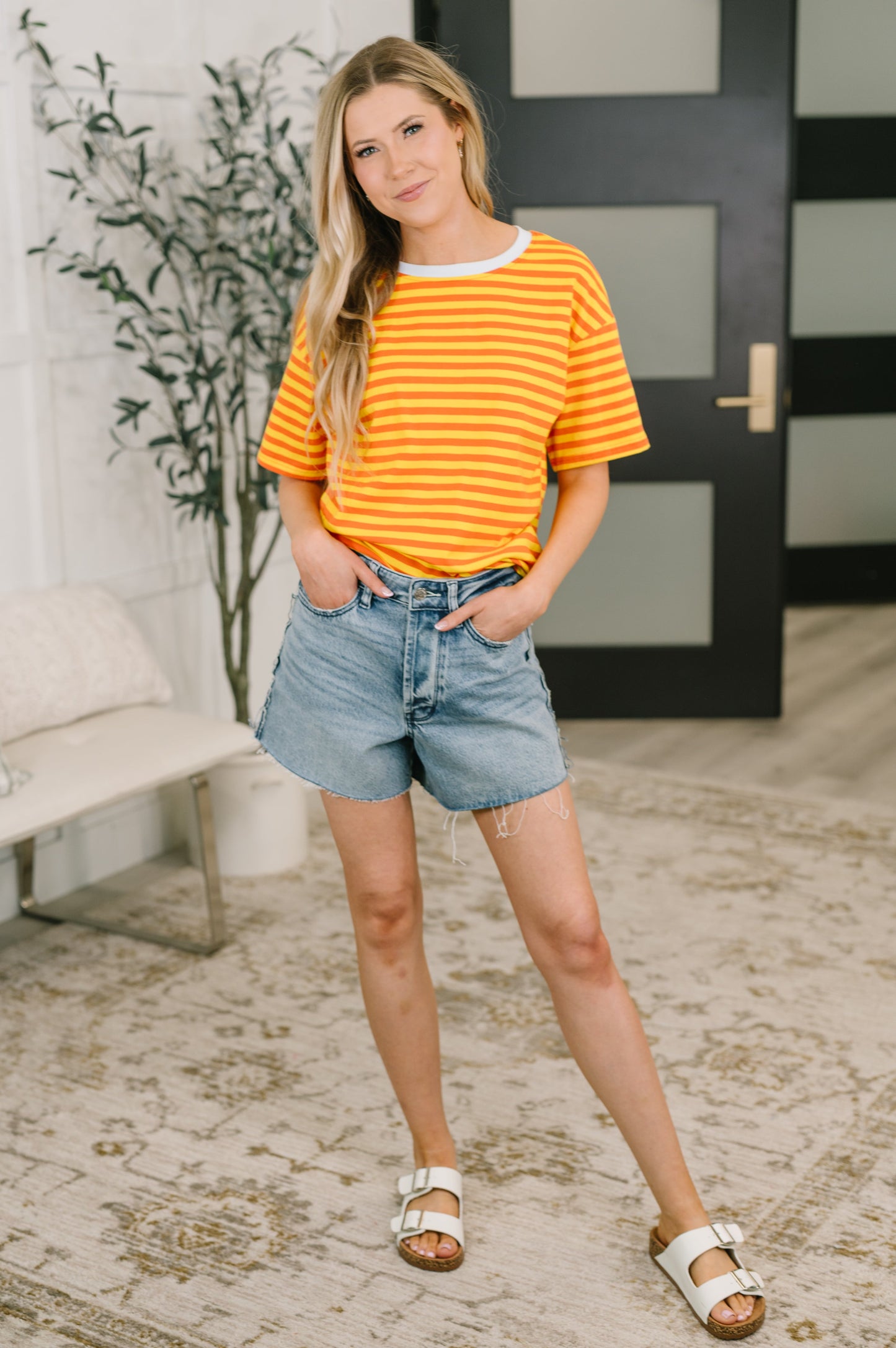 Woman wearing a striped shirt and denim shorts standing indoors.