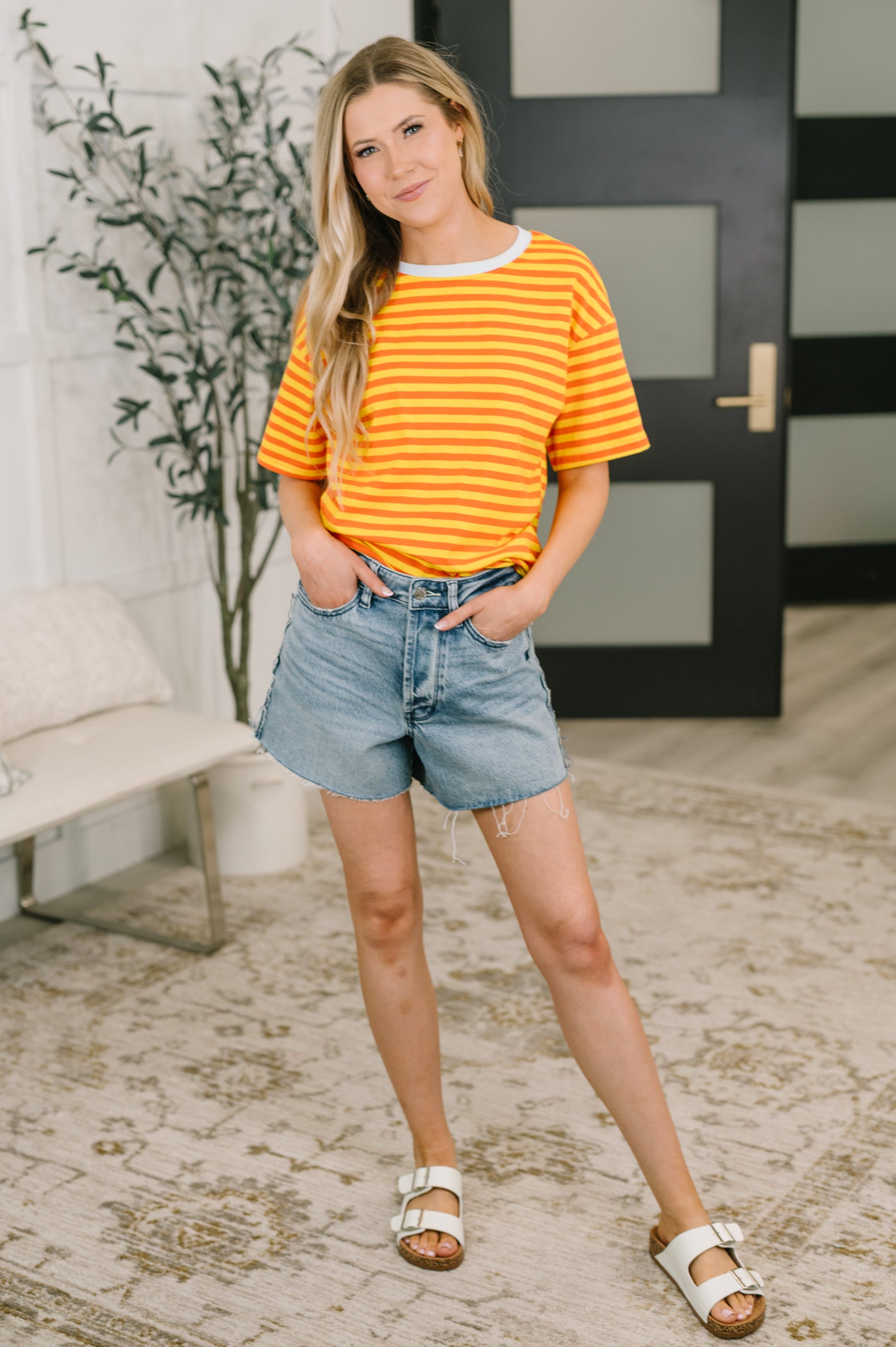 Woman wearing a striped shirt and denim shorts standing indoors.
