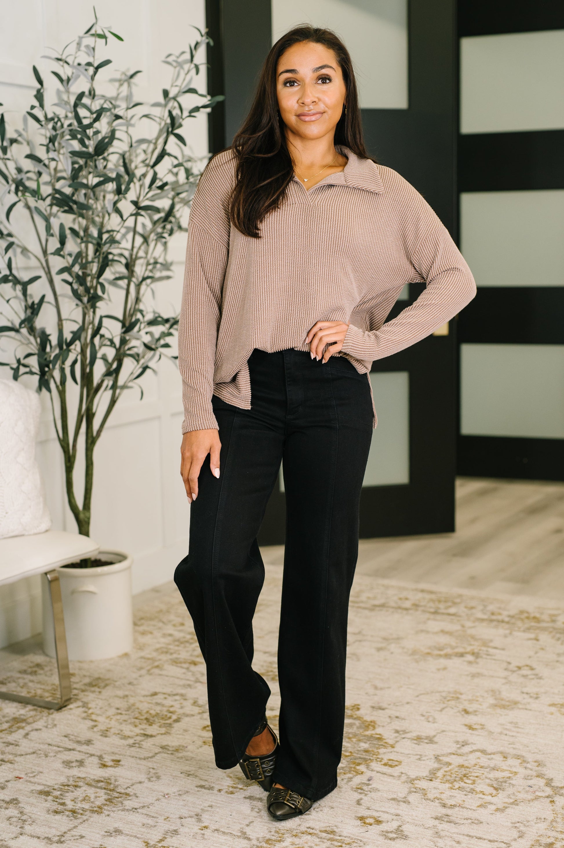 Woman wearing a beige sweater and black pants in an indoor setting