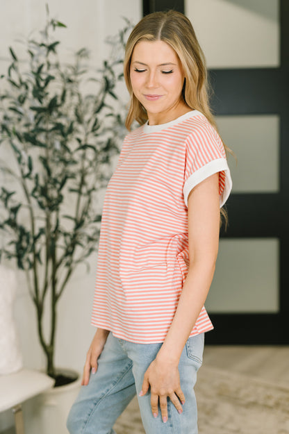 Woman wearing a coral striped shirt and blue jeans indoors.