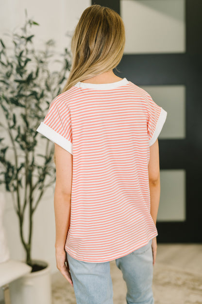 Person wearing a coral striped shirt with light blue jeans indoors.