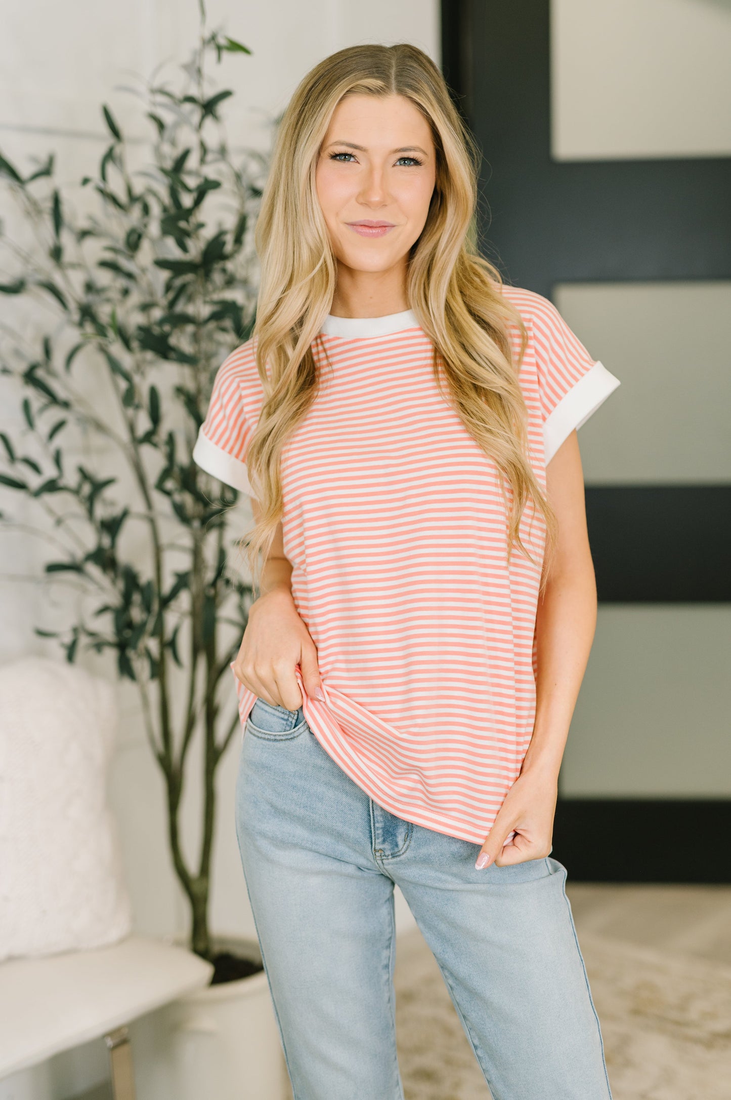 Woman wearing a coral striped shirt and light blue jeans indoors.