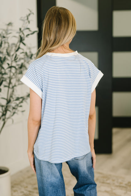 Person wearing a striped shirt and jeans standing in a room with a plant and decorative wall.