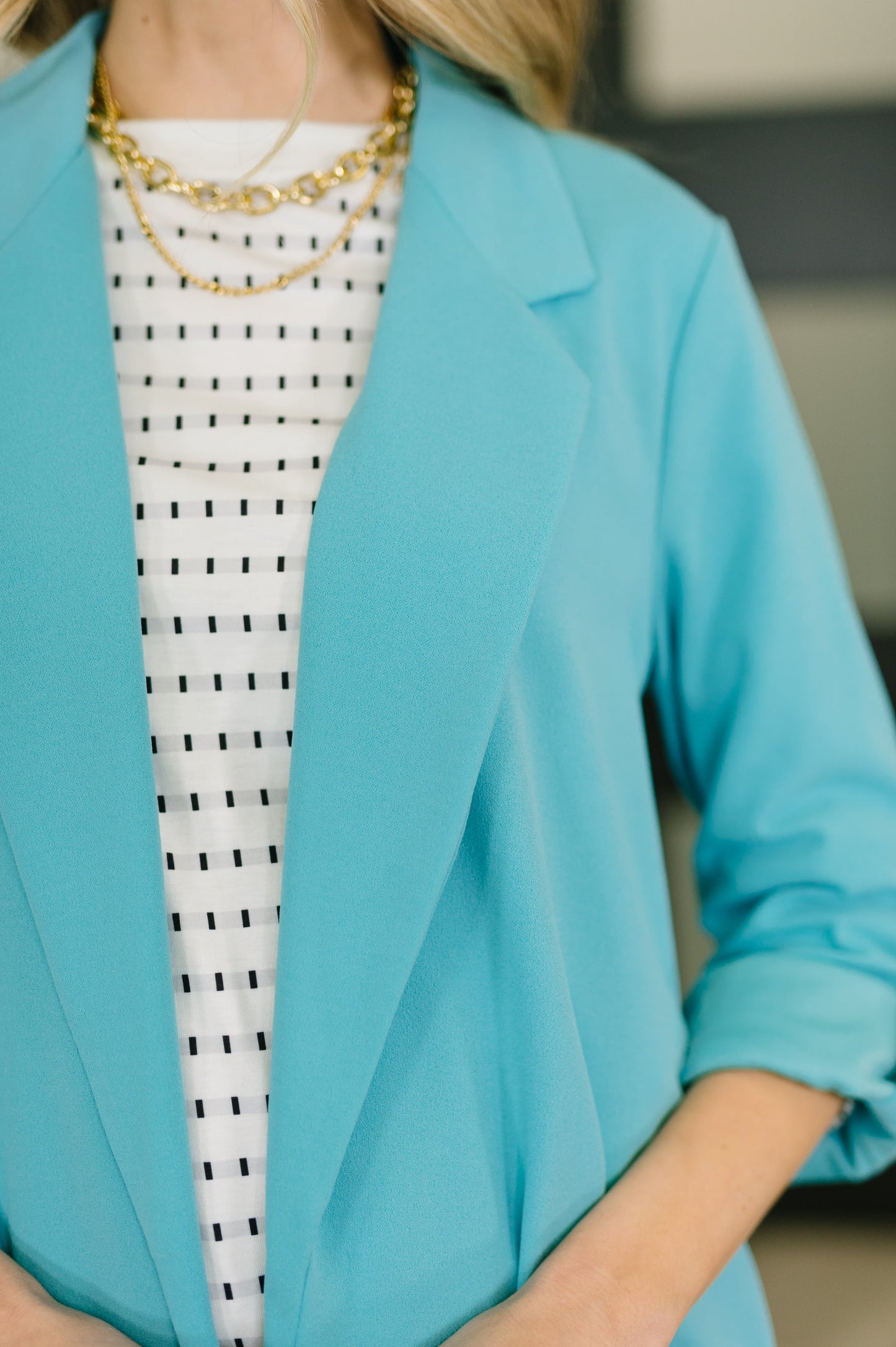 Person wearing a turquoise blazer over a black and white patterned dress.