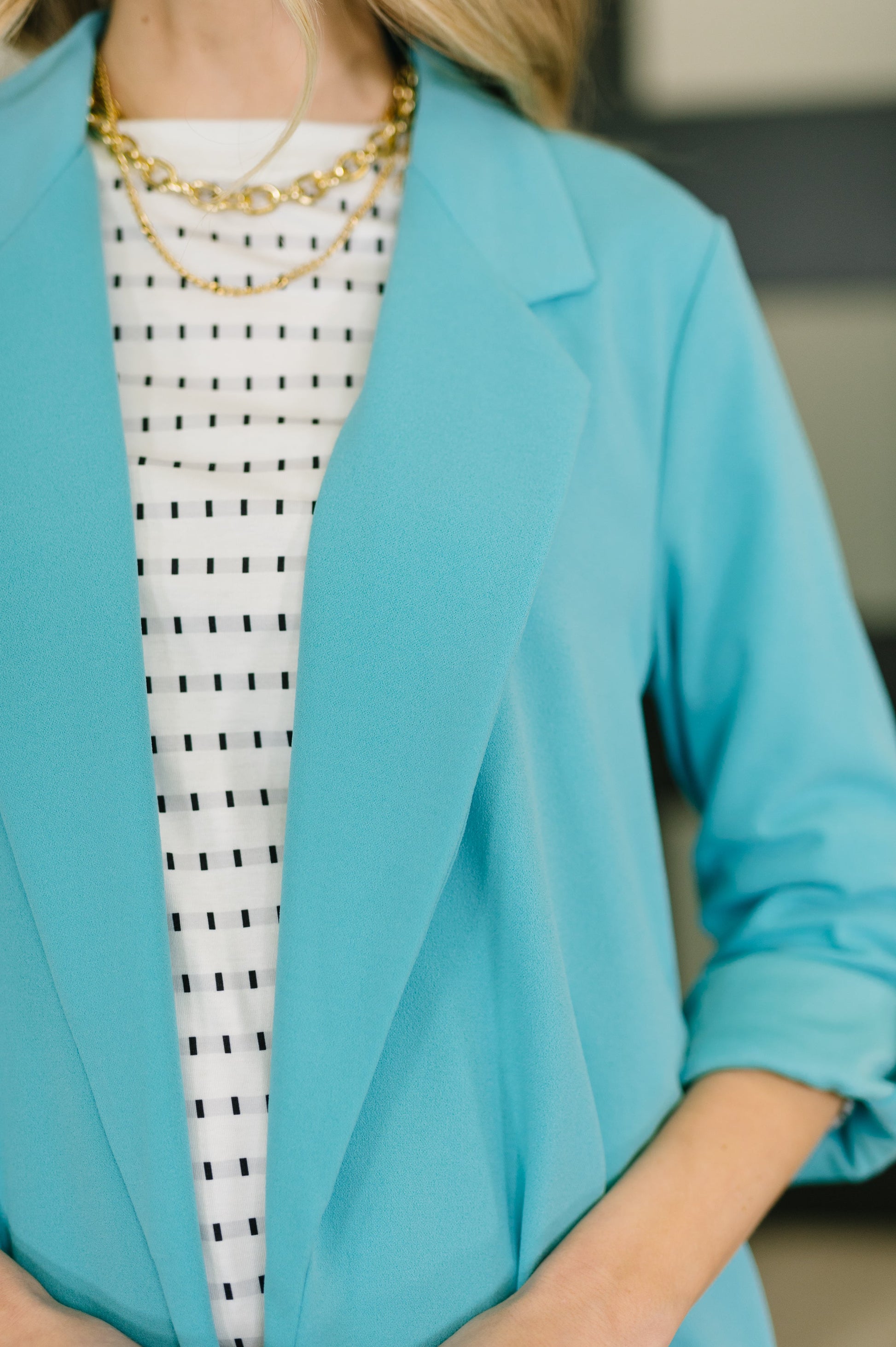 Person wearing a turquoise blazer over a black and white patterned dress.