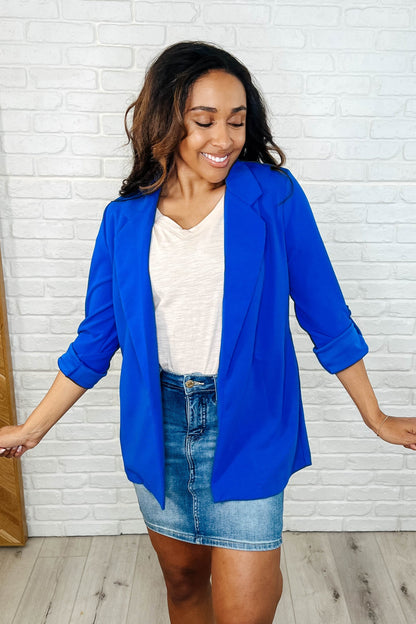 A woman wearing a royal blue open front blazer with a white top and a denim skirt.