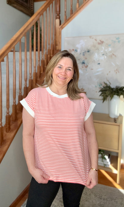 Woman wearing a coral striped shirt standing in a home setting with a staircase and decor.