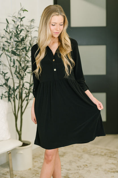 Woman wearing a black dress in an indoor setting with a plant and bench in the background.