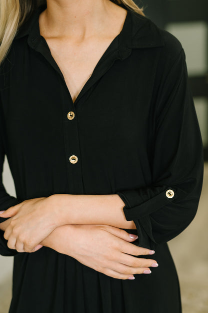 Close-up of a person wearing a black dress with gold buttons.