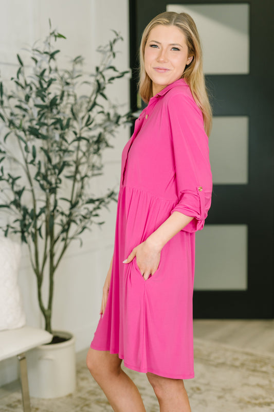 Woman wearing a pink dress standing indoors with a plant in the background