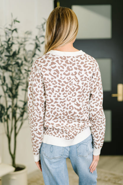 Person wearing a leopard print sweater and light blue jeans indoors.
