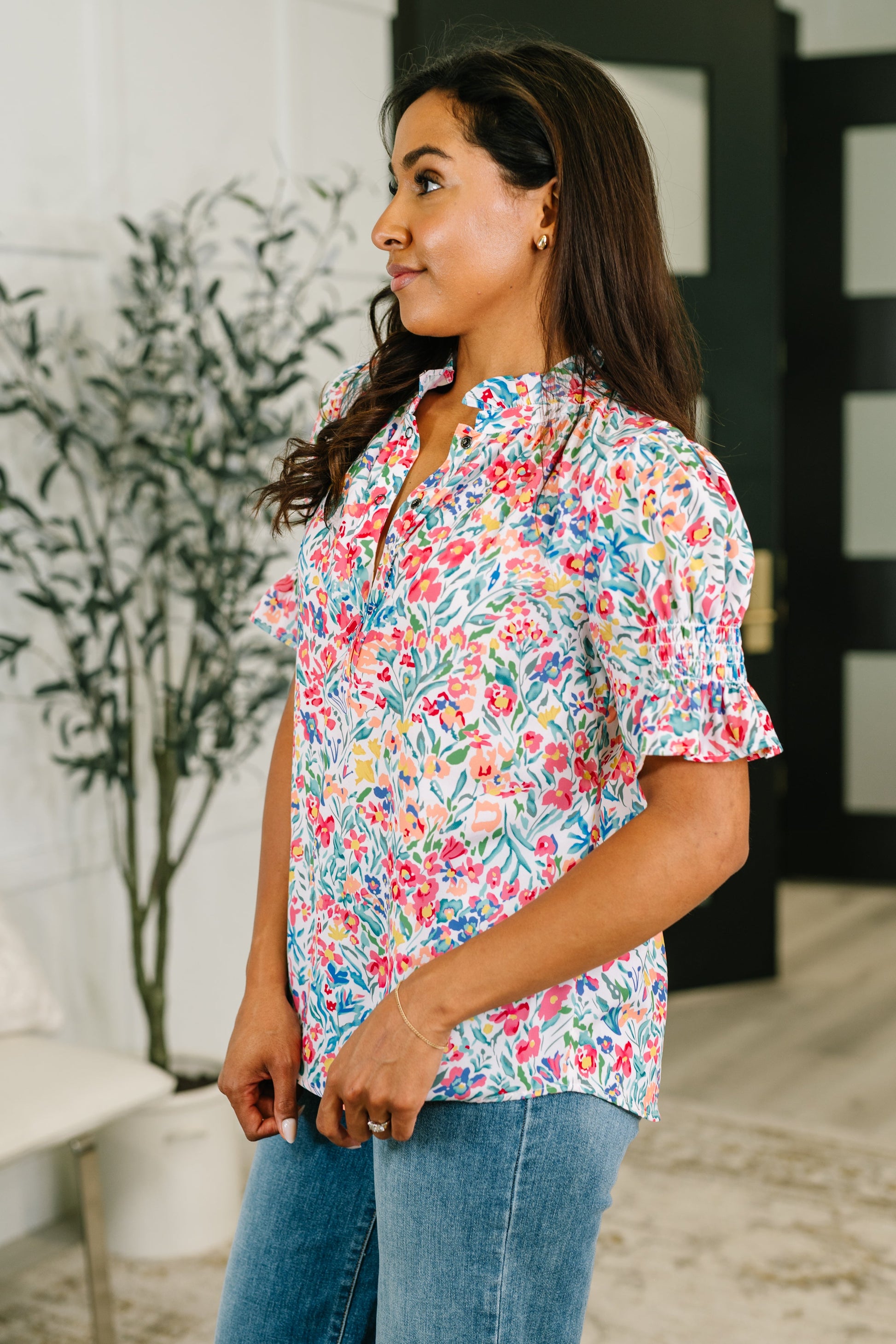 Woman wearing a colorful floral blouse and jeans indoors.