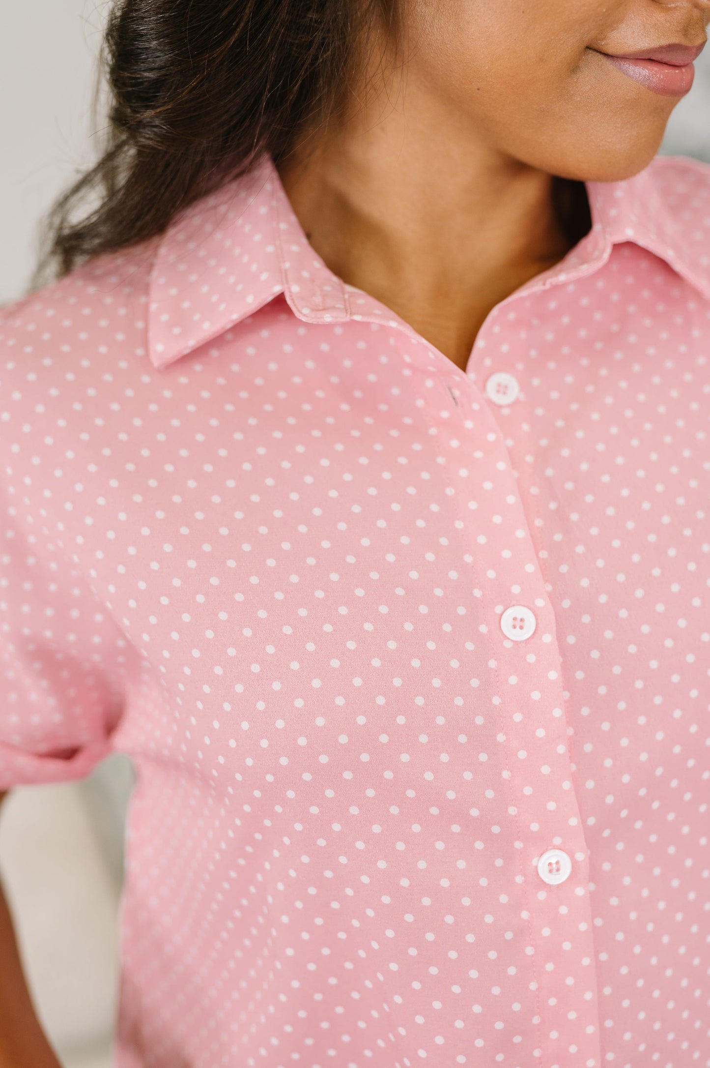 A close-up of a woman wearing a pink short-sleeve button-up shirt with a white micro-dot pattern.