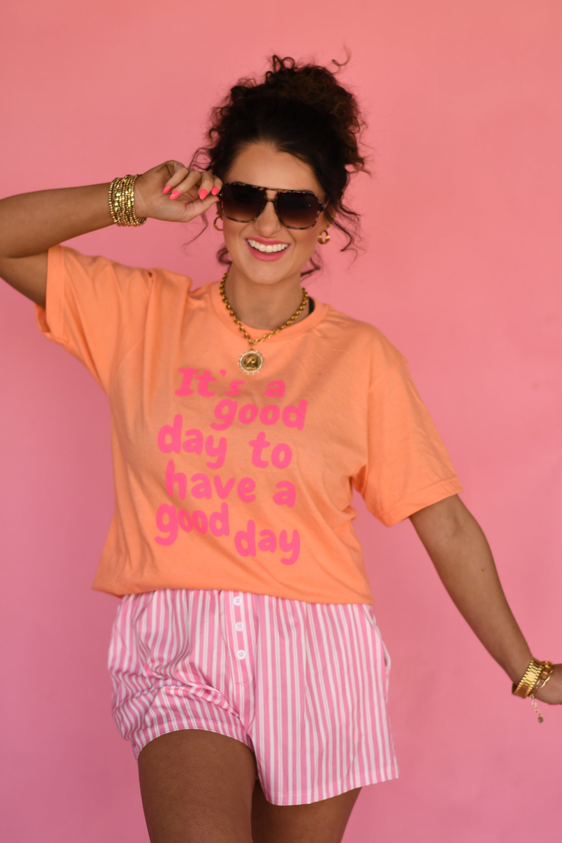 Woman wearing an orange t-shirt with a motivational quote and pink shorts against a pink background