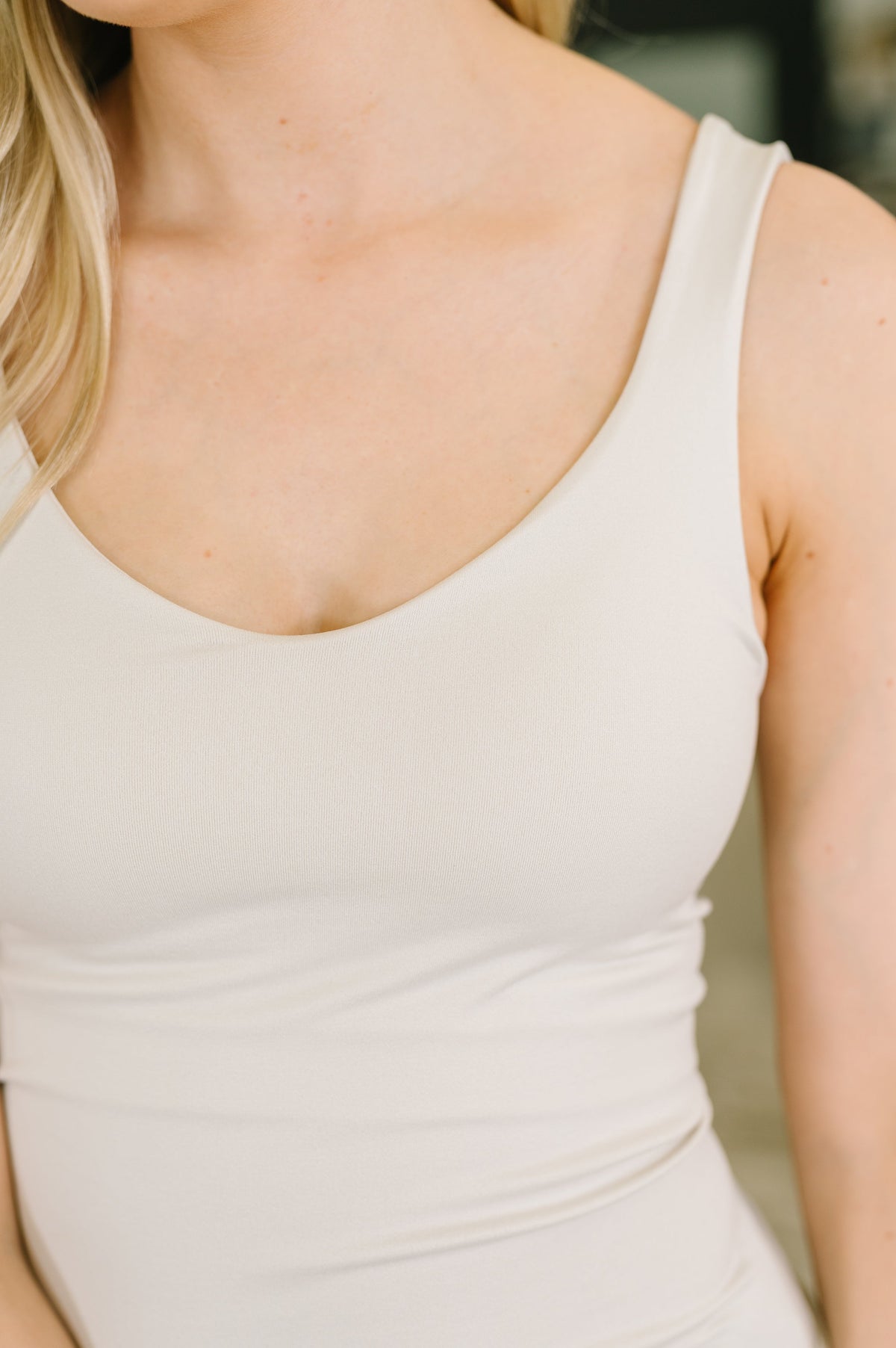 Close-up of a woman wearing a light cream or off-white ribbed tank top, showing the scoop neckline and smooth fabric texture.