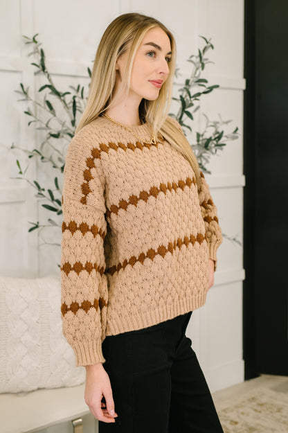 Woman wearing a beige sweater with brown patterns against a white wall.