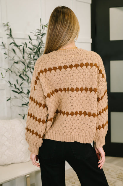 Person wearing a beige sweater with brown stripes in a room with a plant and white wall.