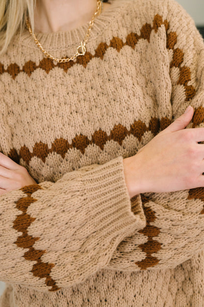 Close-up of a person wearing a brown and beige patterned sweater with a gold necklace.