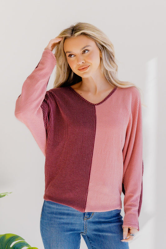 Woman wearing a pink and red ribbed sweater with blue jeans against a white background