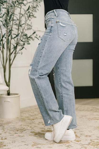 Person wearing light blue jeans and white sneakers in a room with a plant and a black and white abstract painting.