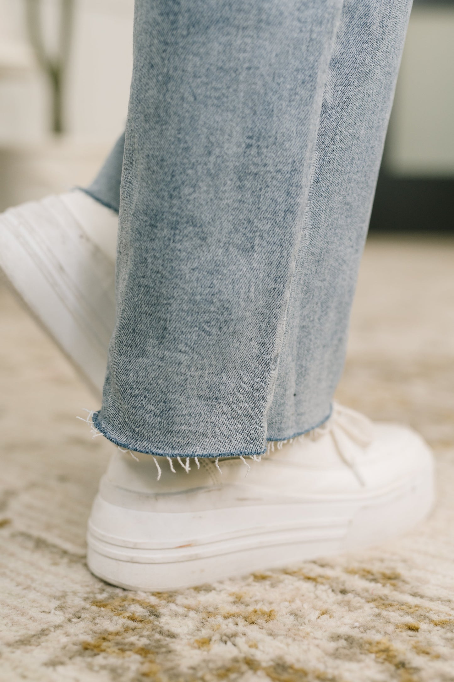 Close-up of light blue jeans and white sneakers on a neutral background