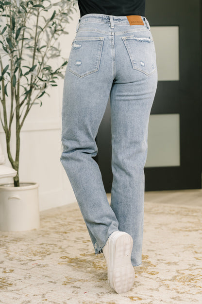 Light blue jeans worn by a person indoors with a plant and wall in the background