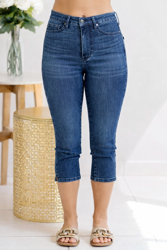 Person wearing blue jeans standing in a minimalistic room with a white wall and wooden stool.