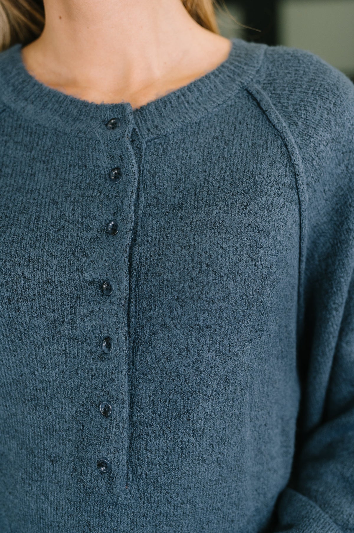 Close-up of a person wearing a textured knit cardigan sweater in a muted slate blue color, featuring a buttoned front closure.