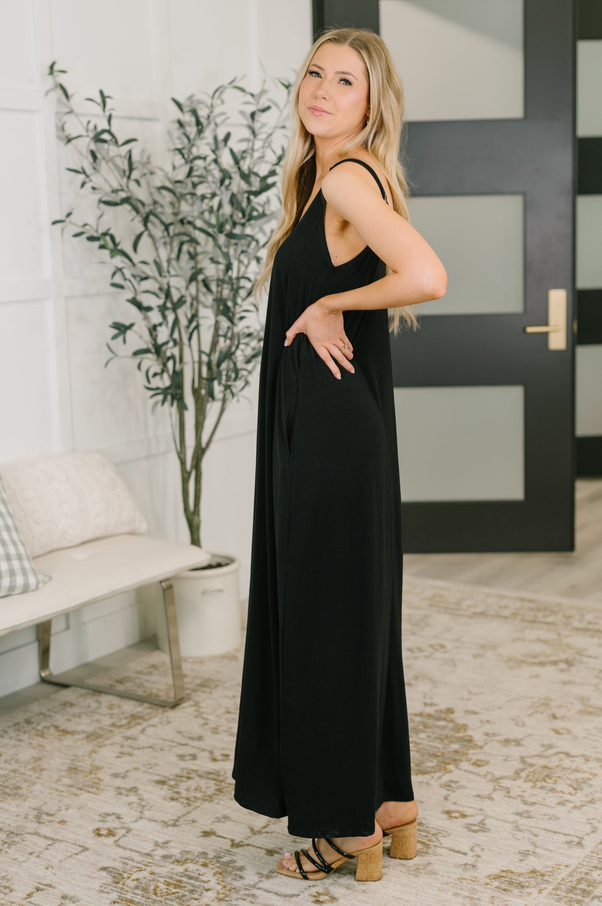 Woman in a black dress standing in a room with a plant and door in the background