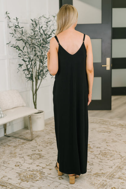 Woman wearing a black dress standing in a room with a plant and door in the background