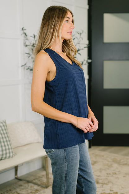 Woman wearing a navy blue sleeveless top and jeans in a living room setting.