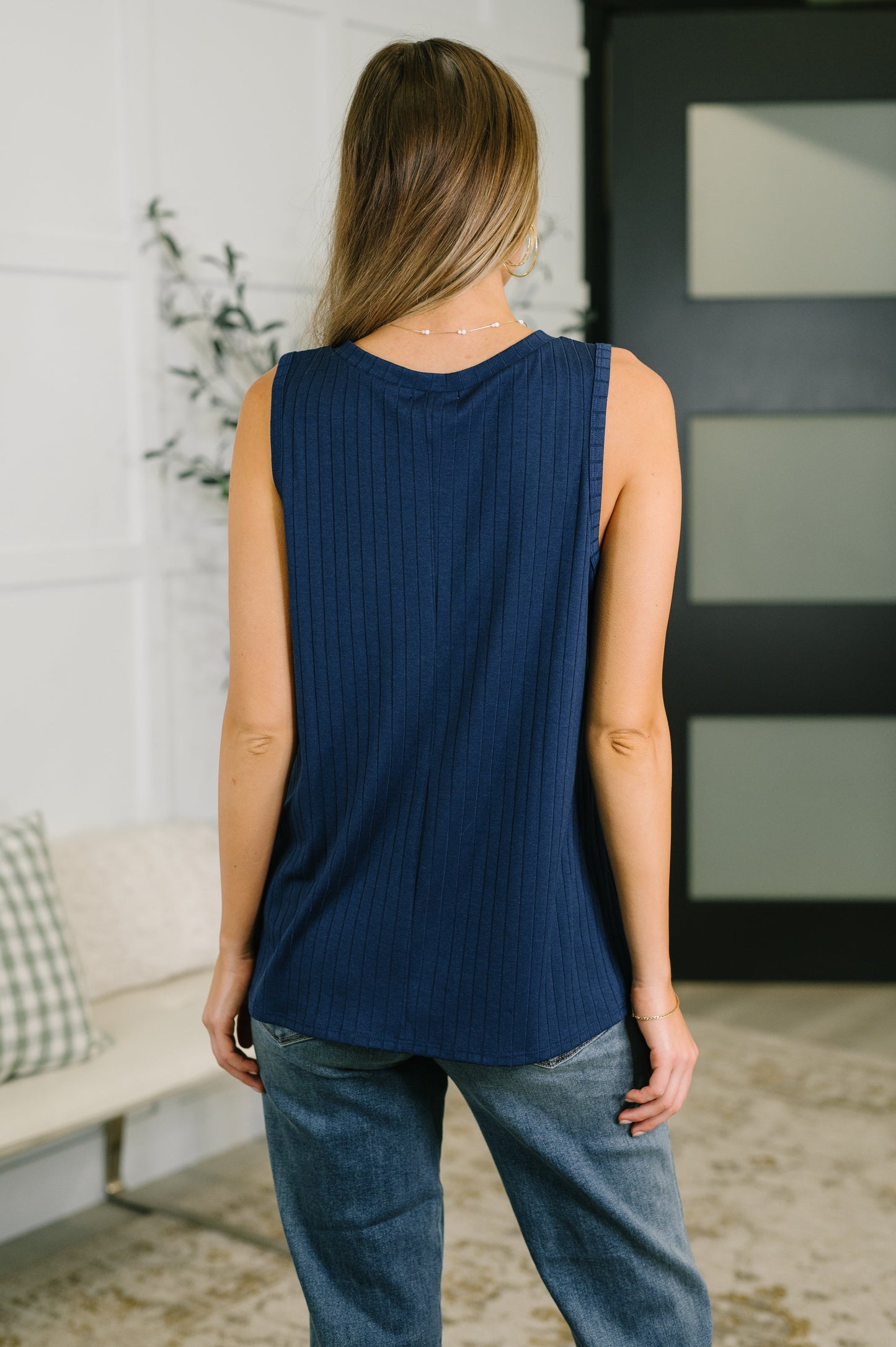 Woman wearing a navy blue sleeveless top and jeans in a living room setting.