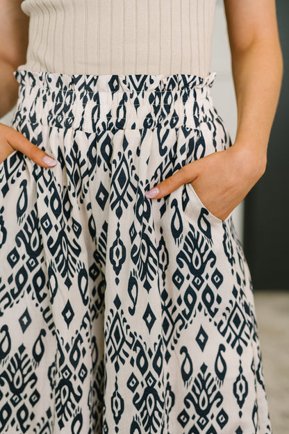 Close-up of a person wearing a cream-colored pleated skirt with a navy blue geometric ikat pattern, paired with a ribbed cream top.