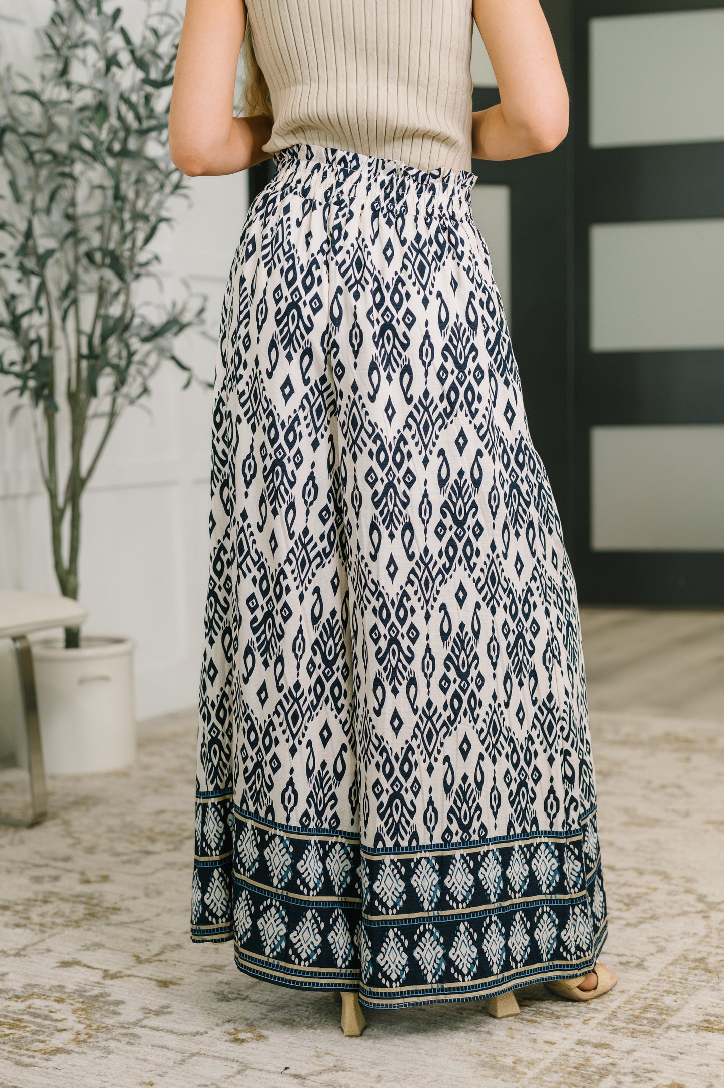 A person shown from the back wearing a cream ribbed knit top and a long, wide-leg pleated skirt with a navy blue and cream geometric ikat pattern and a decorative border.
