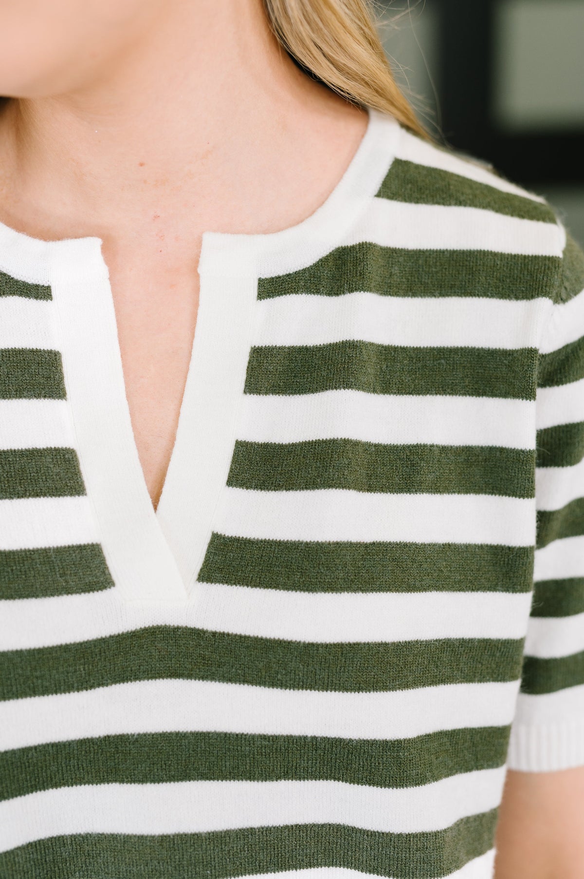 Close-up of a person wearing a short-sleeve knit top with horizontal green and white stripes and a split V-neckline.