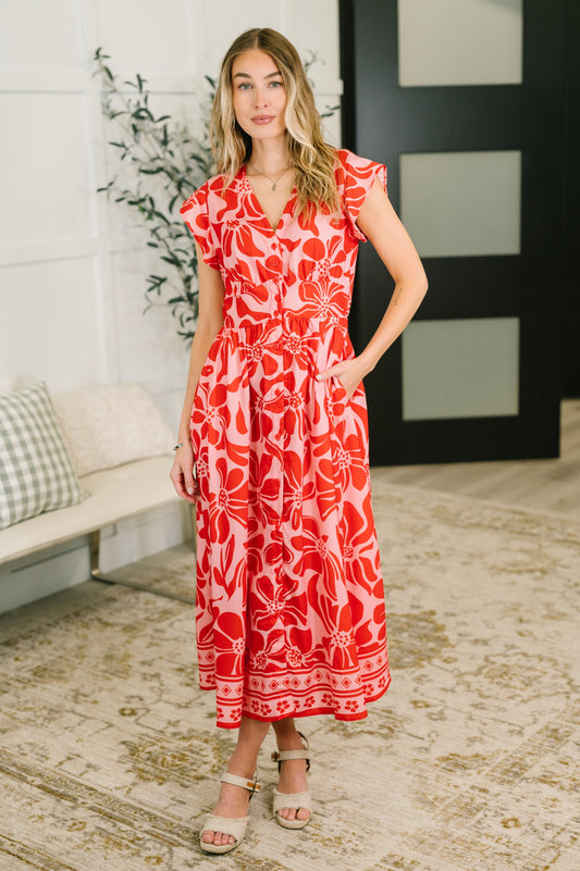 Woman wearing a red floral dress standing in a room with a couch and plant.