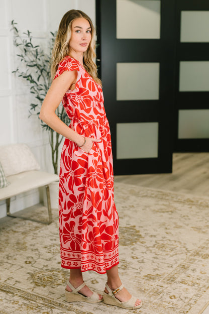 Woman wearing a red floral dress standing in a room with a plant and a black and white abstract painting.