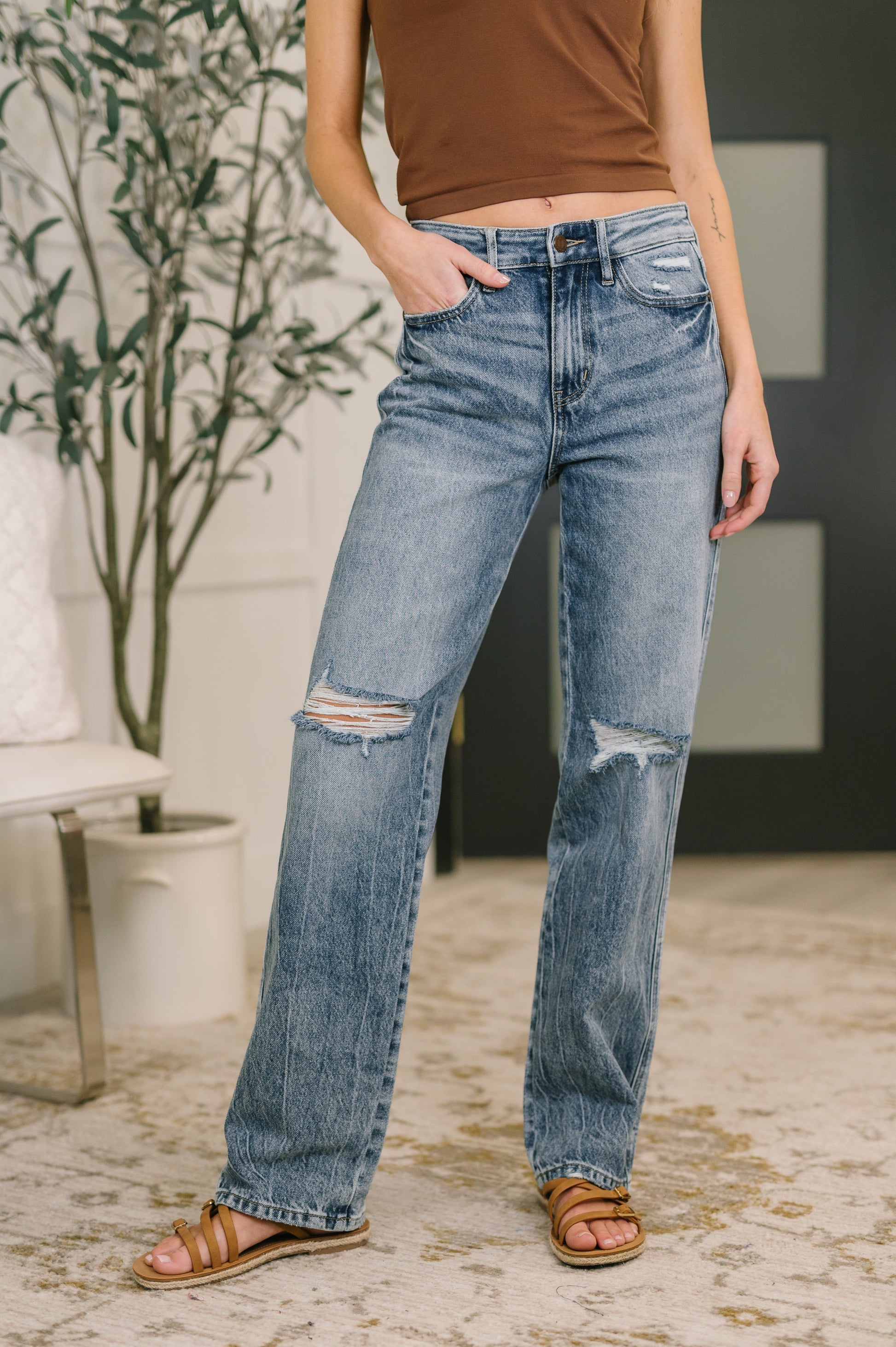 Person wearing distressed blue jeans and a brown top indoors.