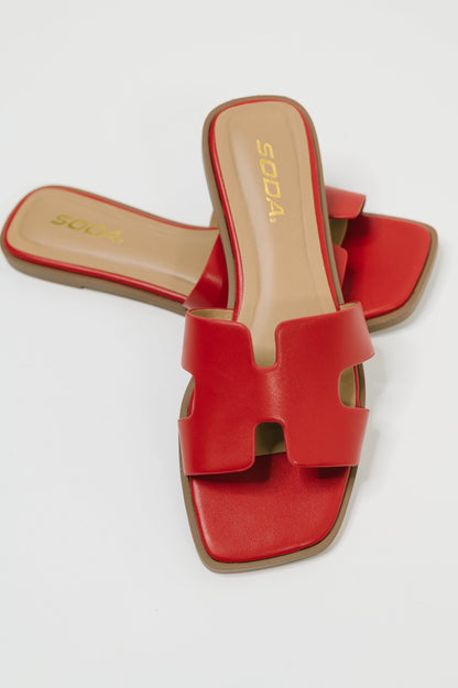 Red leather slide sandals with a wide cutout strap, shown from a top-down angle on a light gray background. The brand name 'SODA' is visible in gold on the tan insole.