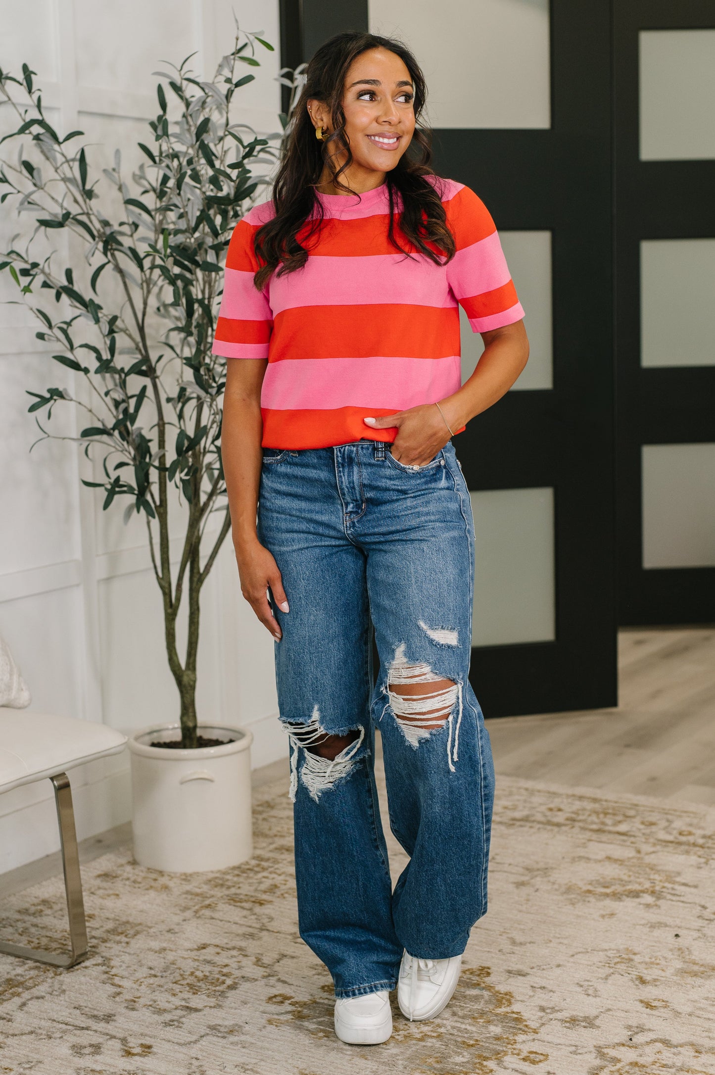 Woman wearing a striped shirt and jeans standing indoors with a plant in the background