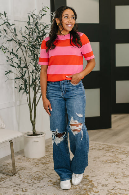 Woman wearing a striped shirt and jeans standing indoors with a plant in the background