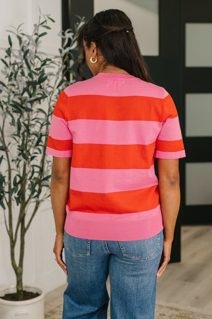Person wearing a red and pink striped sweater with blue jeans, standing indoors.