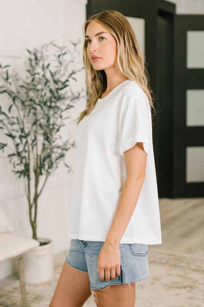 Woman wearing a white t-shirt and denim shorts in an indoor setting with a plant in the background