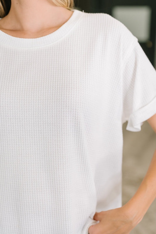 Close-up of a person wearing a white textured t-shirt with a blurred background