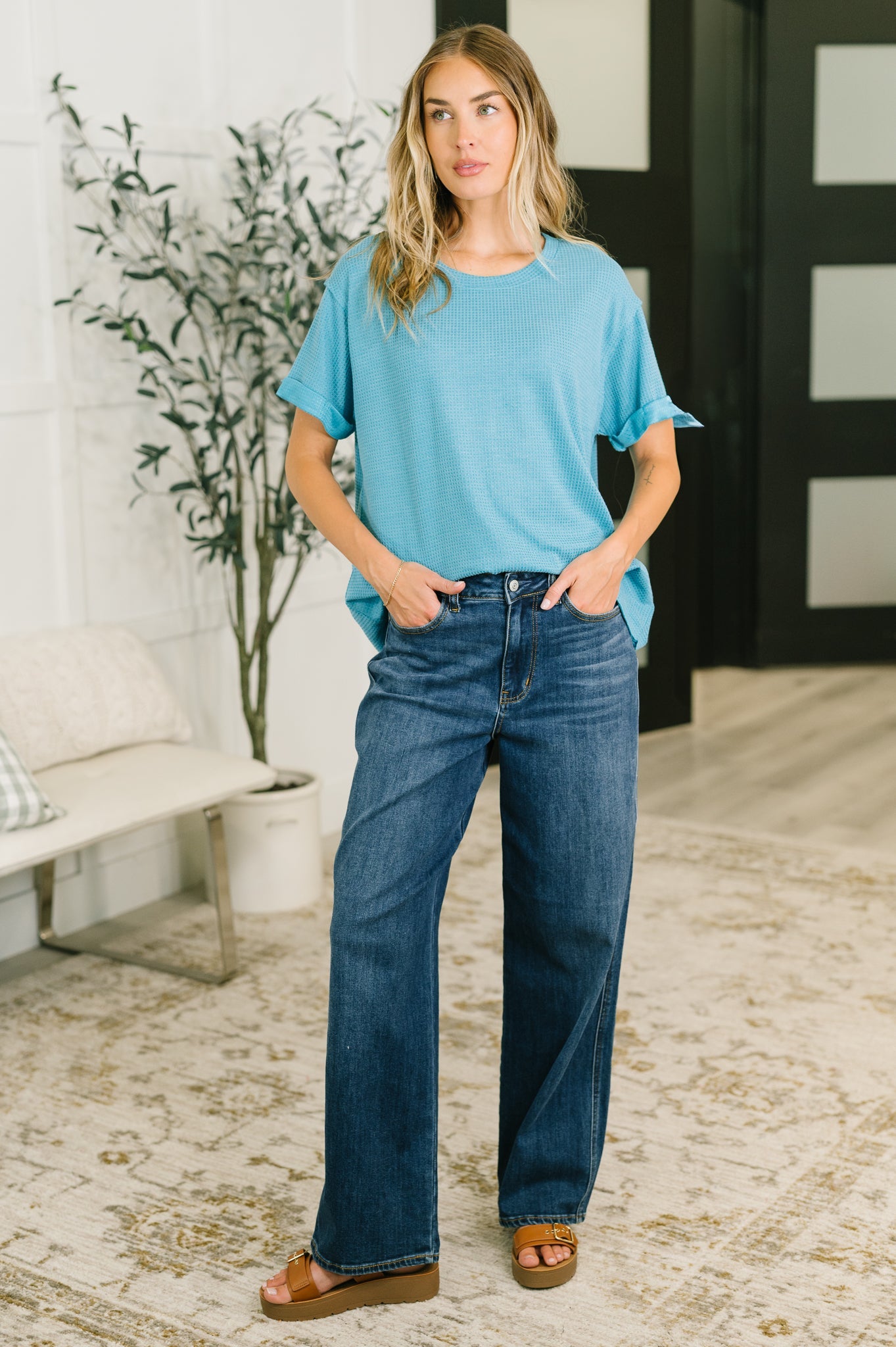 Woman wearing a blue t-shirt and jeans standing in a living room.